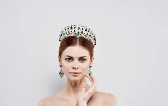Молодая женщина в роскошной короне с изумрудами на светлом фоне