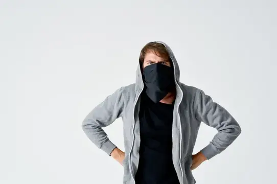 Мужчина в сером капюшоне и чёрной маске стоит руки в боки