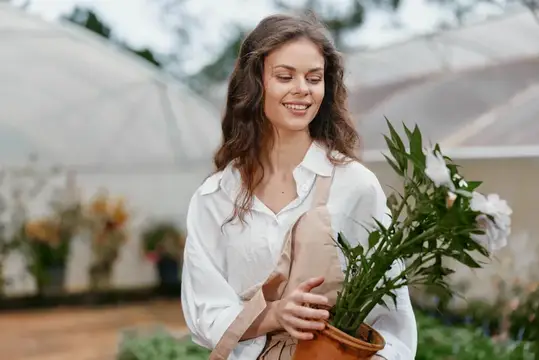 Улыбающаяся девушка с горшком цветов в теплице