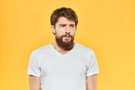 Задумчивый бородатый мужчина в белой футболке на жёлтом фоне