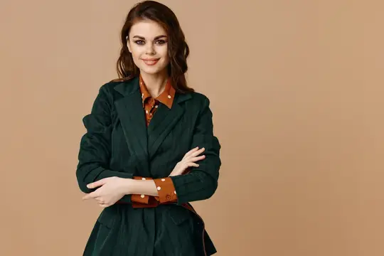 Улыбчивая темноволосая девушка в зелёном плаще на бежевом фоне