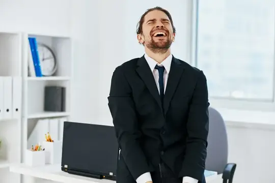 Мужчина в костюме громко смеётся в светлом офисе