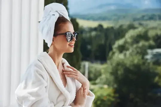 Улыбающаяся женщина в халате и солнечных очках на балконе с видом на горы