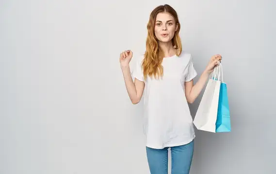Женщина в белой футболке и джинсах держит в руках пакеты