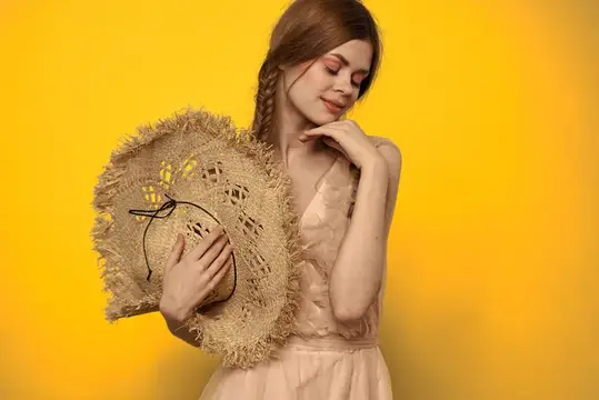 Женщина в соломенной шляпе, держащая руки на желтом фоне