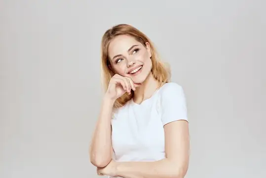 Милую блондинку в белой футболке, жестикулирующую руками, сняли в стиле лайфстайл на светлом фоне