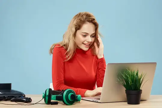 Улыбающаяся блондинка в красном работает за ноутбуком