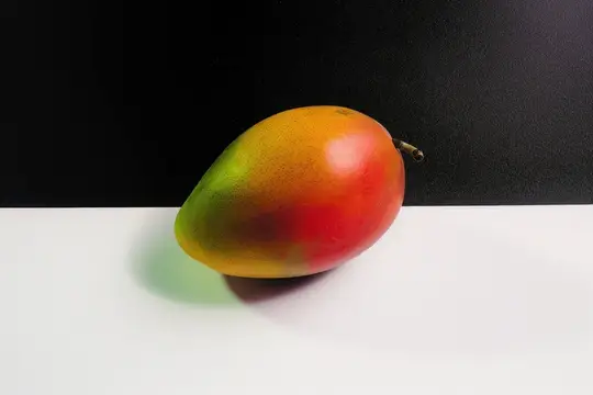 Спелый манго с красно-зелёным боком на белом фоне