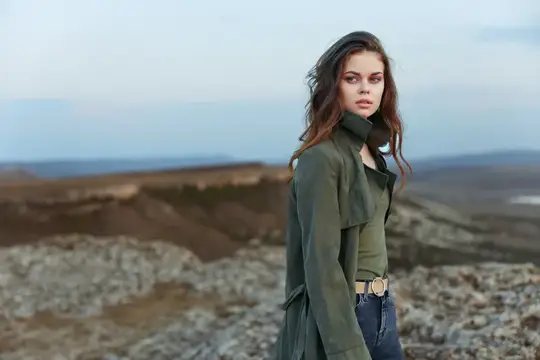 Женщина в зеленой куртке наслаждается живописным горным видом с вершины холма
