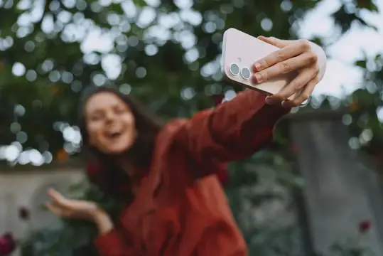Улыбающаяся девушка в красном делает селфи на смартфон в саду