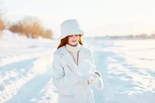 Рыжеволосая девушка в белом пальто и шапке на зимней прогулке