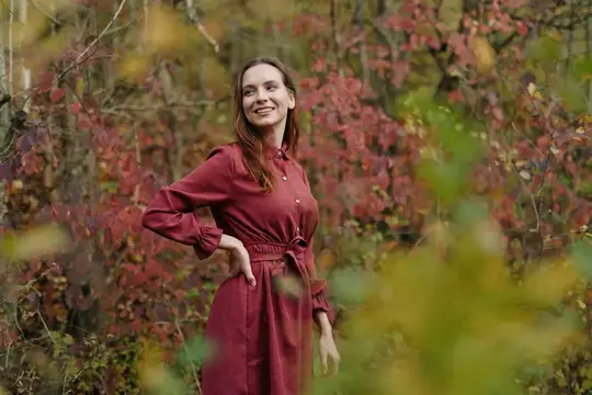 Улыбающаяся девушка в бордовом платье осенью в лесу