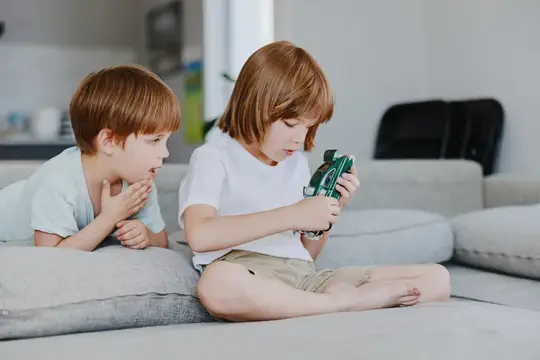 Два рыжеволосых мальчика играют с игрушечной машинкой на диване