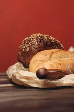 Мучные изделия, буханка хлеба в бумажной упаковке, острый нож и деревянный стол