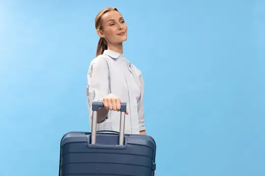 Молодая женщина с чемоданом мечтательно смотрит вверх на голубом фоне