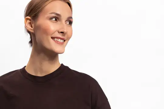 Улыбающаяся светловолосая женщина в коричневой футболке смотрит в сторону