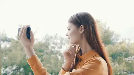 Женщина на улице держит в руках телефон и делает селфи