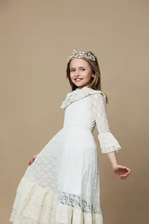 Очаровательная юная девушка в красивом белом кружевном платье и изящной короне демонстрирует счастье и уверенность