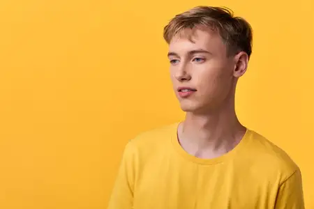 Мужчина-модель в желтой футболке позирует с задумчивым взглядом на ярком желтом фоне