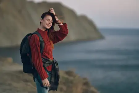 Женщина с рюкзаком, в красном свитере, модель на фоне гор и океана
