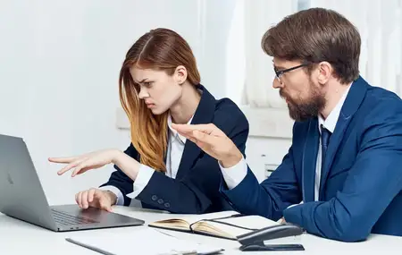 Бизнесмен и симпатичная женщина в костюмах на работе, в офисе с открытым ноутбуком и цветком в горшке