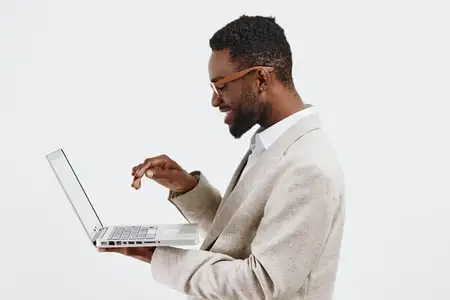 Улыбающийся мужчина уверенно работает с ноутбуком на однотонном фоне
