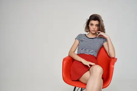Симпатичная женщина в очках сидит на красном стуле на светлом фоне, стиль жизни