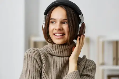 Молодая женщина в наушниках слушает музыку на смартфоне, сидя дома
