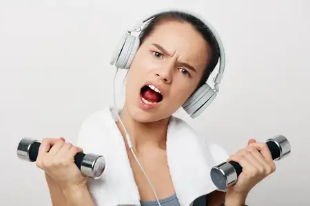 Динамичный спортивный портрет женщины-атлета в наушниках, сжимающей гантели и потеющей от усилий, передающий преданность, силу и спортивный настрой во время интенсивной тренировки