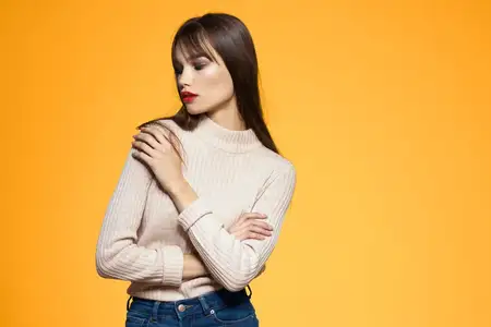 Симпатичная брюнетка с красными губами и в модной одежде в студии на жёлтом фоне