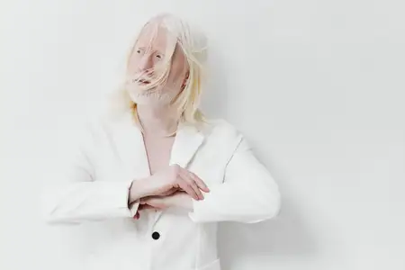Яркий модный портрет человека с длинными, естественно уложенными белыми волосами, одетого в шикарный белый костюм