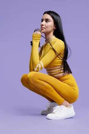 Молодая женщина, энтузиастка спортивного фитнеса, в желтом спортивном костюме приседает, держа скакалку