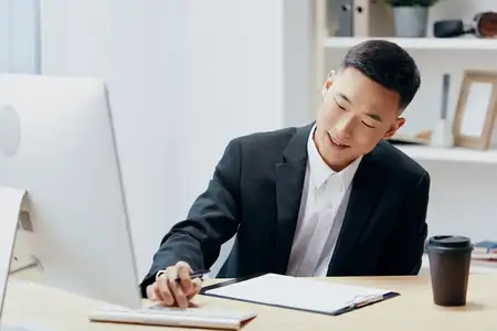 Азиатский мужчина работает за компьютером с чашкой кофе, эмоции в офисе