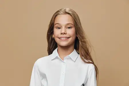Юная девушка улыбается, одетая в белую рубашку, с длинными волосами на коричневом фоне