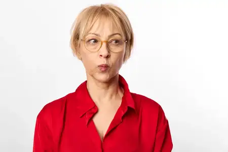 Женский портрет в очках, красной блузке и студийном освещении, короткие светлые волосы и сосредоточенное лицо, нейтральный фон с белым задником, прямой взгляд, спокойное уверенное серьезное настроение