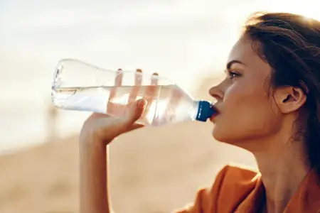 Женщина пьет воду из бутылки на открытом воздухе