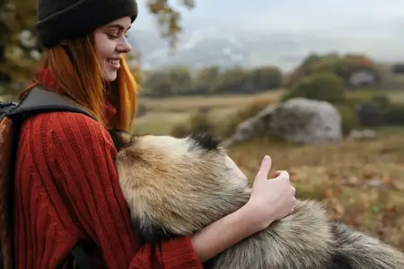 Веселая женщина-туристка играет с собакой на свежем воздухе среди природы