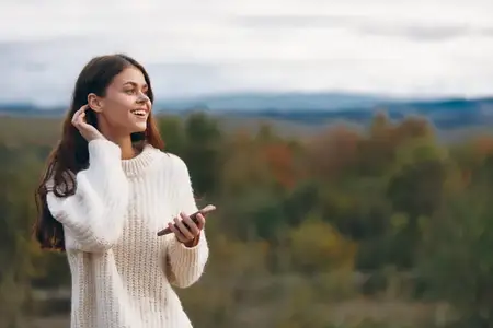 Связь женщины в горах по телефону: улыбающаяся искательница приключений, наслаждающаяся свободой природы