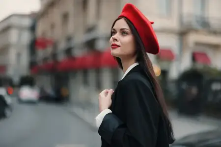 Портрет красивой модной женщины, стоящей на улице на фоне города в стильной одежде, с красными губами и красным беретом