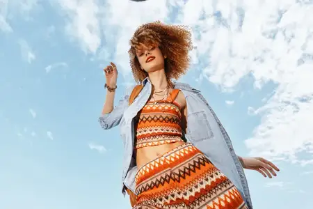 Улыбающаяся женщина с рюкзаком беззаботно танцует на пляже под открытым небом, наслаждаясь моментом