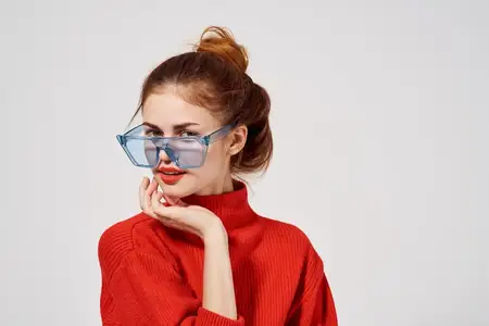 Модная женщина в красном свитере и синих очках на светлом фоне