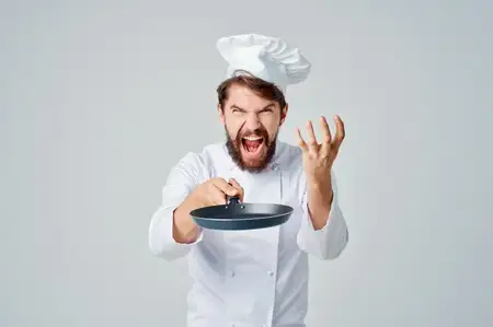 Бородатый мужчина-повар с кухонной утварью на светлом фоне