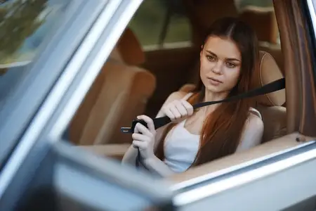 Молодая женщина застёгивает ремень безопасности в автомобиле, излучая уверенность и осознание безопасности, в окружении мягкого естественного света и тёплых тонов, что идеально подходит для…