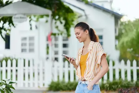 Веселая молодая женщина пользуется смартфоном на улице в яркой обстановке