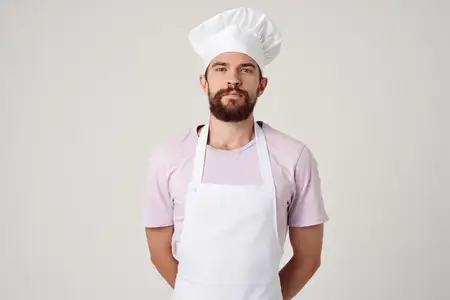Бородатый мужчина в белом фартуке готовит на кухне ресторана