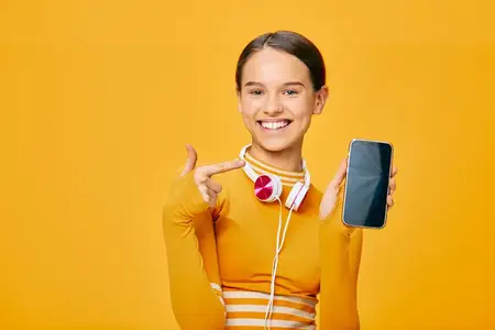 Портрет подтянутой спортсменки, указывающей на экран смартфона, в наушниках, готовая к тренировке, на ярком цветном фоне