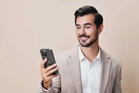 Уверенный мужчина в белом костюме, счастливо улыбаясь, держит смартфон и делает селфи