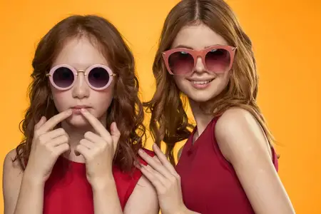 Весёлая мама и дочка в солнцезащитных очках, стиль жизни, дружба, семья, жёлтый фон, студия