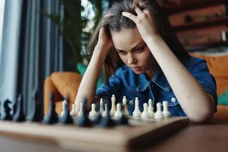 Молодая женщина чувствует разочарование и стресс во время игры в шахматы за столом