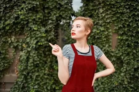 Привлекательная женщина с короткой стрижкой стоит на улице на фоне кустов